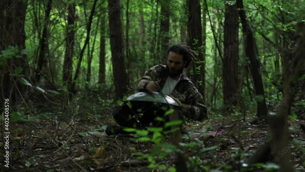 Man playing hand pan in between the trees in forest Man playing hand pan in between the trees in forest