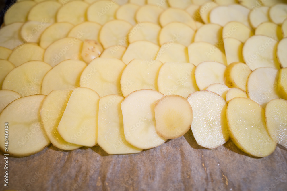 Raw sliced potatoes lined-up on a baking tray