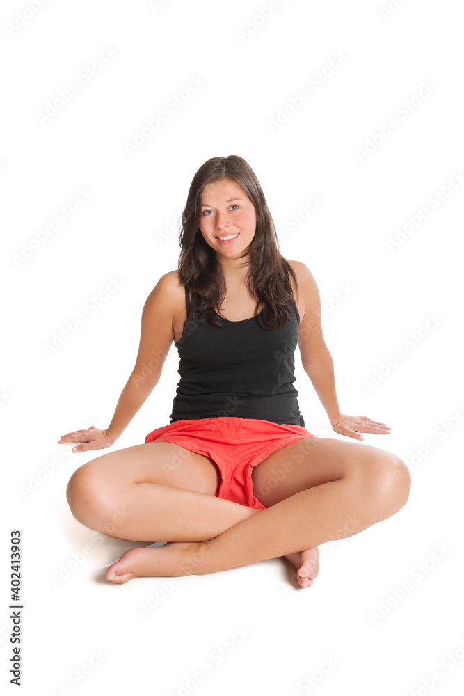 Beautiful young woman wearing red shorts and black top sitting in front of white studio background 
