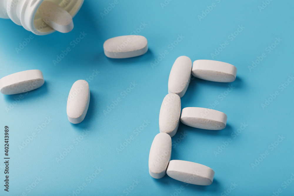Vitamin E pills fell out of a white jar on a blue background. The letter E is an inscription.