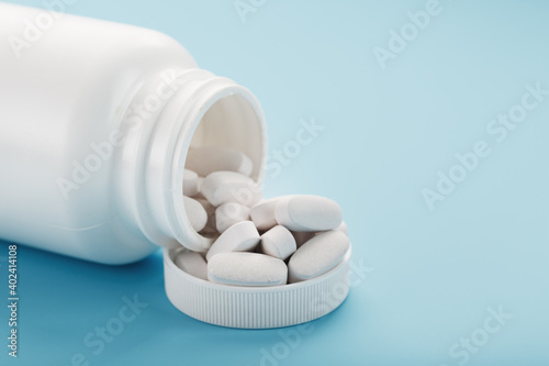 White capsules with vitamins and minerals in the form are poured from a jar on a blue background.
