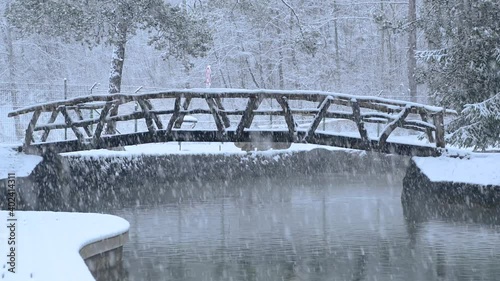 River flowing through stone canal with a wooden bridge in fairy tale winter landscape. Snowstorm in campground Sobec, Slovenia. Amazing view of snowflakes falling. Static shot, real time
