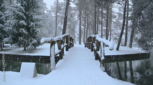 River flowing through stone canal with a wooden bridge in fairy tale winter landscape. Snowstorm in campground Sobec, Slovenia. Amazing view of snowflakes falling. Static shot, real time, wide angle