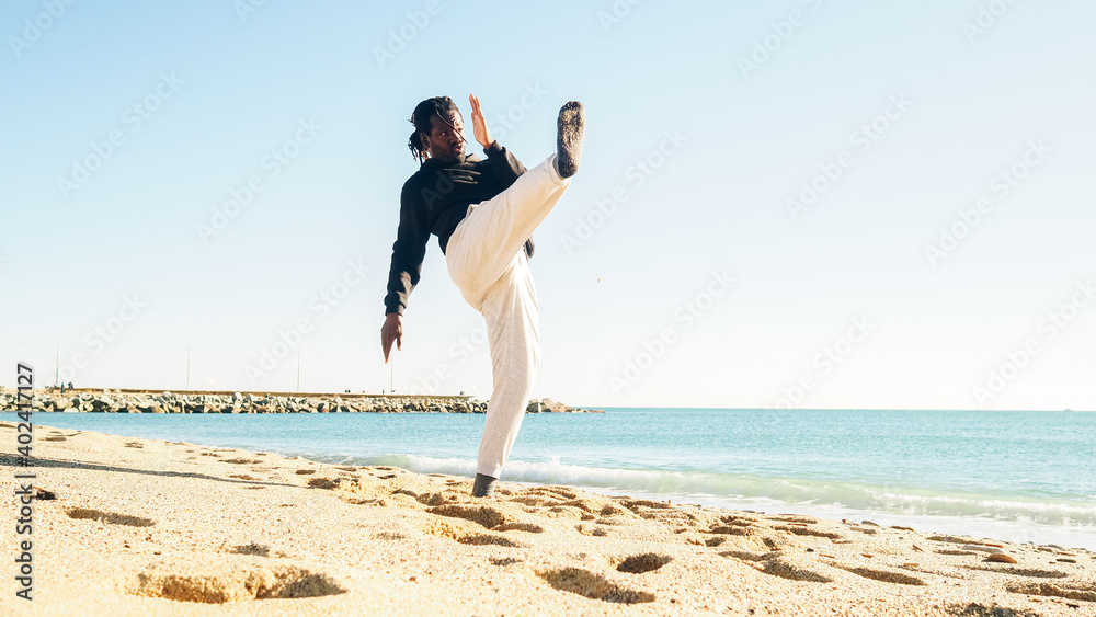 Afro man with dreadlocks training martial arts on a beach launching a kick. Personal motivation, self defense Afro man with dreadlocks training martial arts on a beach launching a kick. Personal motivation, self defense