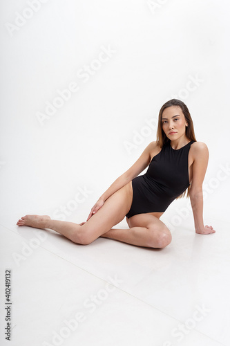 sexy asian woman with long hair posing in black lingerie on white studio background with bare feet. attractive female sitting on floor with her knees bent. model tests of skinny lady in bodysuit