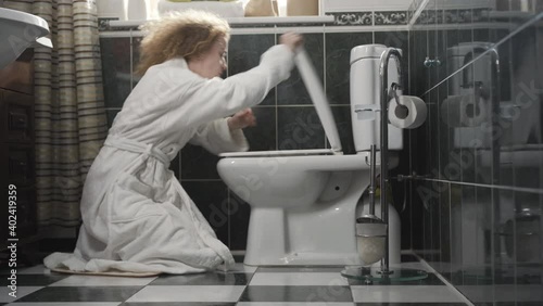 Side view of sick or pregnant woman opening wc and vomiting in toilet. Wide shot of unhealthy Caucasian lady in white bathrobe in bathroom. Intoxication or pregnancy concept. photo