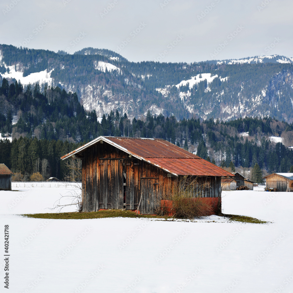 Braune Scheune mit rostigem Dach im Winter im Schnee bei Oberstdorf in Bayern, Deutschland