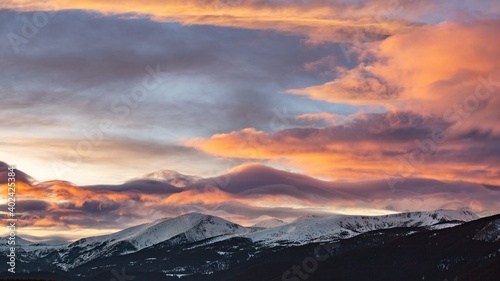 Sunset over snowy peaks in Rila Mountain, Bulgaria. Attractive orange cloudy sky, white slopes, natural landscape panoramic view. Perfect winter conditions for travel, sport recreation and tourism.