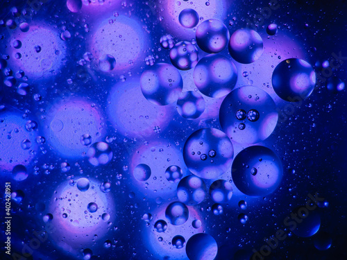 Makroaufnahme von Öltropfen in Wasser mit blauem Hintergrund. Sieht aus wie eine ferne Galaxie.