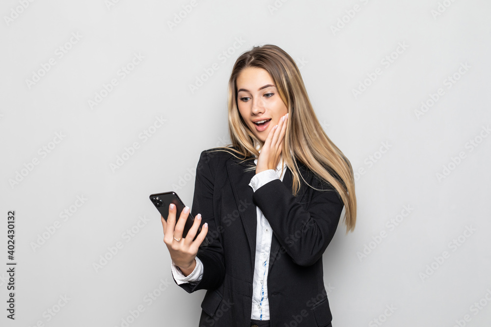 Portrait of surprised and impressed business woman with widened eyes and opened mouth, stunned on phone while standing against white background. Girl uses some app Portrait of surprised and impressed business woman with widened eyes and opened mouth, stunned on phone while standing against white background. Girl uses some app