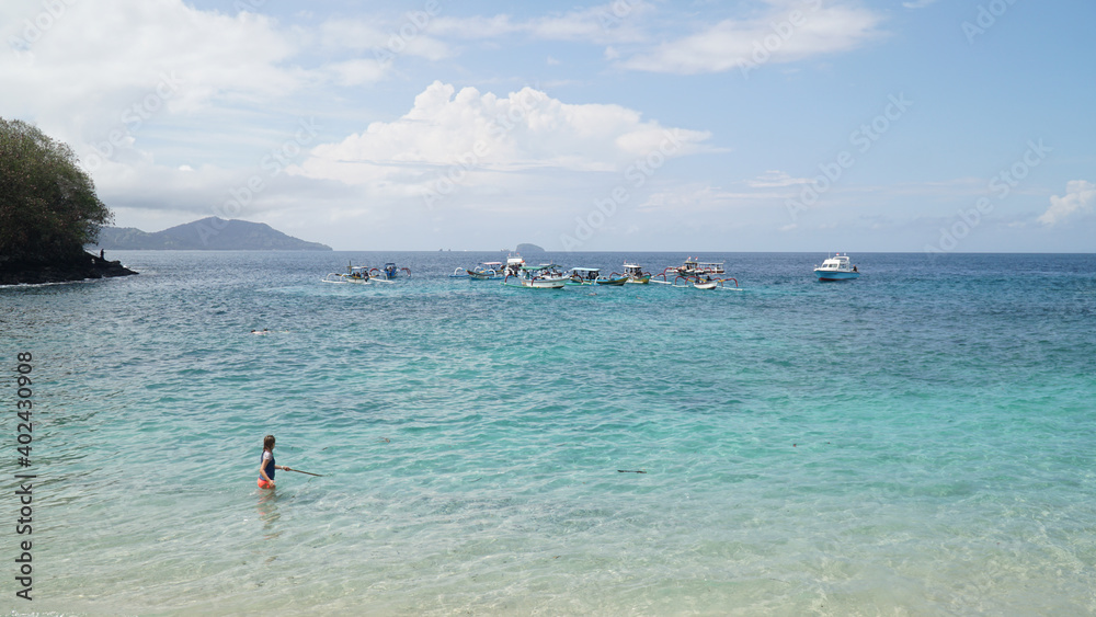 Boats and people visiting Tropical Blue Lagoon Beach near Bali in Indonesia.