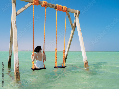 Young woman sat on a swing in the ocean - white sand and turquoise water of the Giftun islands, Egypt