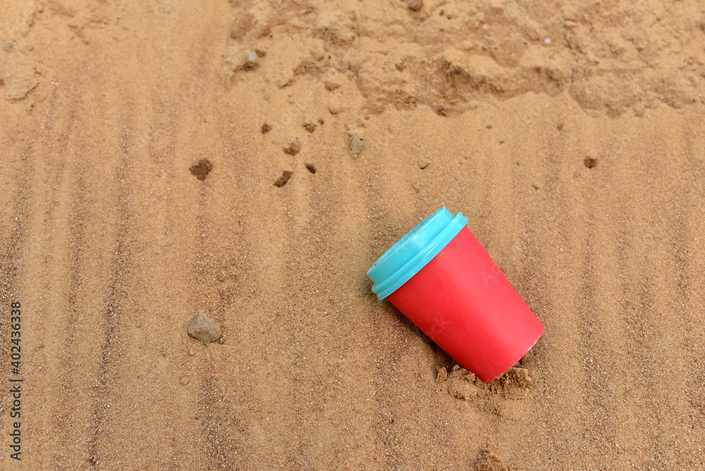 Discarded Paper coffee cup on sand at beach. Disposable coffee cup on sandy background. The problem of environmental pollution. Pile of abandoned garbage, including food waste, fast food packaging Discarded Paper coffee cup on sand at beach. Disposable coffee cup on sandy background. The problem of environmental pollution. Pile of abandoned garbage, including food waste, fast food packaging