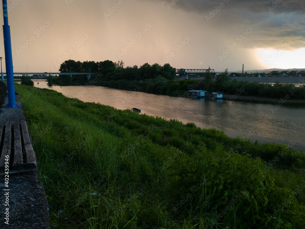 Storm cumulonimbus cloud with heavy rain or summer shower, severe weather and sun glow behind rain. Landscape with Sava river with island in Bosanski Brod, Bosnia and Herzegovina