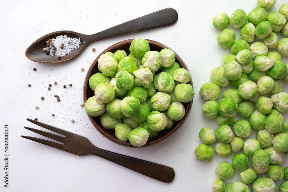 Brussels sprouts lies on the table and in a wooden bowl, next to them lie a wooden fork, a spoon and salt in a spoon