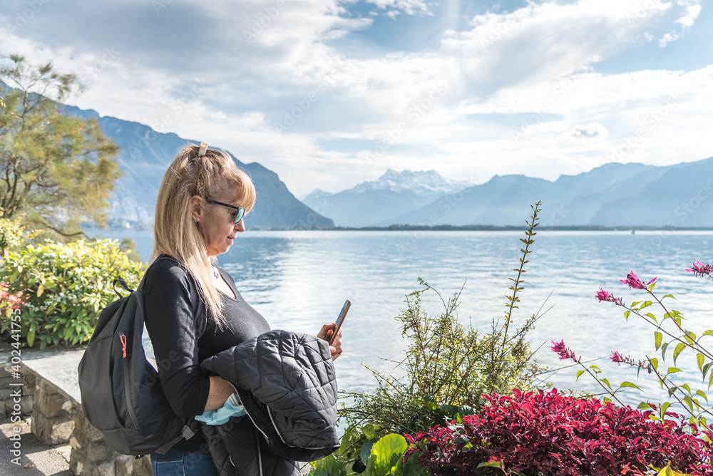 Woman with sunglasses and a bag using her mobile in front of a lake