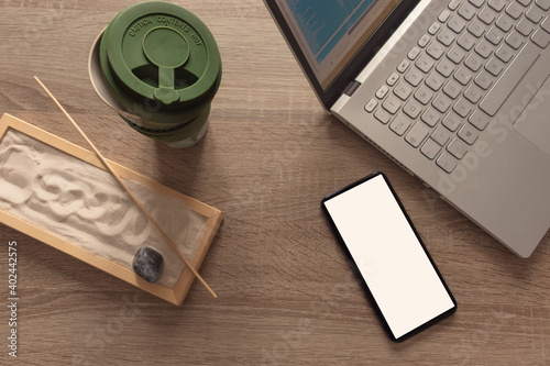 Flat lay, top view of a office table desk. Workshop layout with smartphone, laptop, coffee mug, and zen garden on wooden background. Copy space.