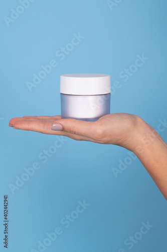 Cropped shot of woman holding jar of moisturizing cream isolated on blue. Background with empty space for your design