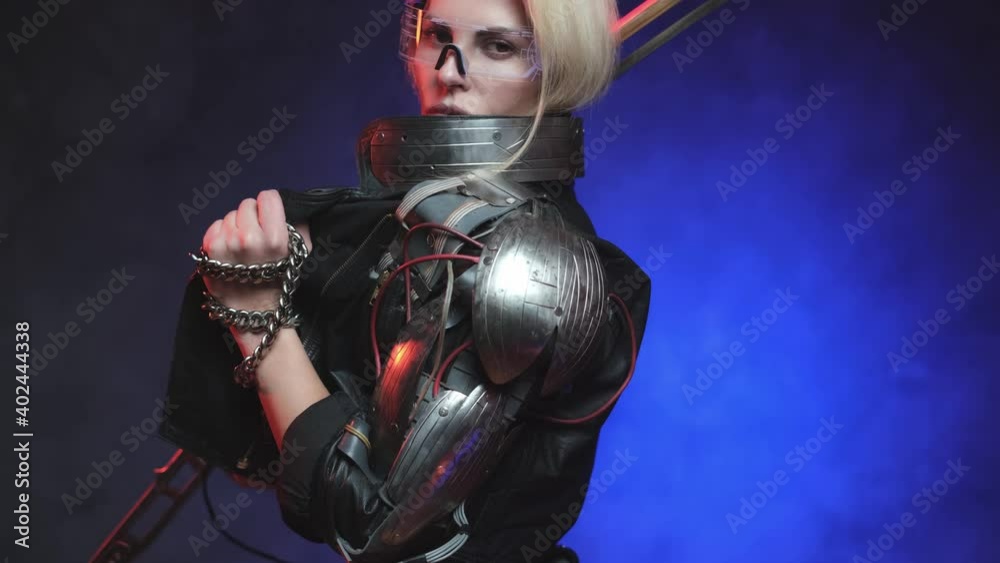 Fantasy portrait of a female warrior from the future with glasses and blond hairs dressed in black leather jacket poses in dark blue background looking at camera and holding chains and steel sword. Fantasy portrait of a female warrior from the future with glasses and blond hairs dressed in black leather jacket poses in dark blue background looking at camera and holding chains and steel sword.
