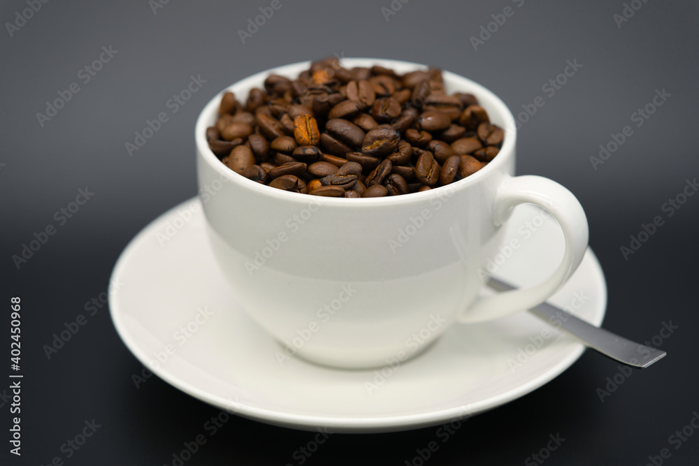 A white cup with aromatic coffee beans with a spoon on black background A white cup with aromatic coffee beans with a spoon on black background