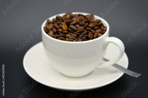 A white cup with aromatic coffee beans with a spoon on black background