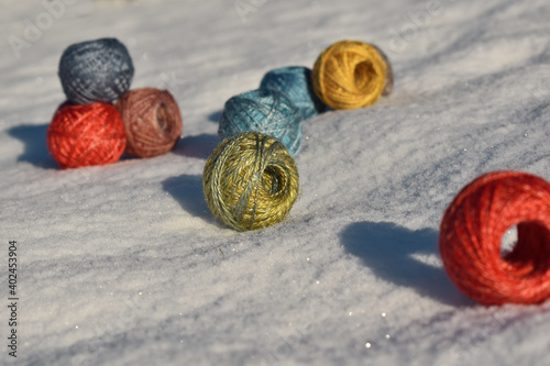 little balls of wool, silk yarn in the snow in sun, colorful in red, blue, yellow, green, purple, background for knitting, weaving 