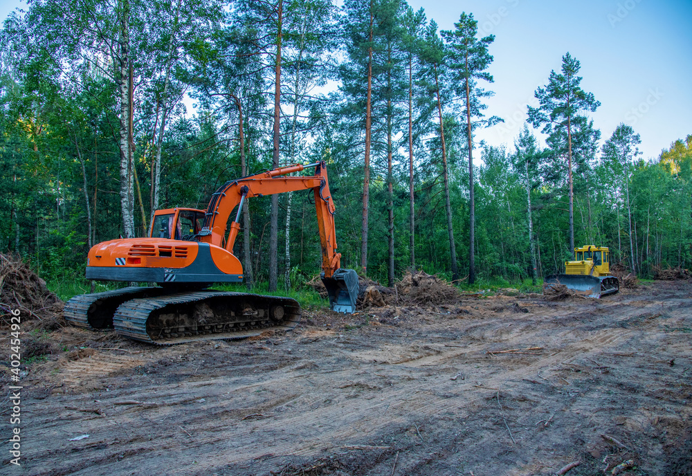 Excavator clearing forest for new development. Orange Backhoe modified for forestry work. Tracked heavy power machinery for forest and peat industry. Logging, road construction in forests Excavator clearing forest for new development. Orange Backhoe modified for forestry work. Tracked heavy power machinery for forest and peat industry. Logging, road construction in forests