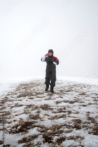 A young man immersed in the mist using the smartphone on a snow-covered mountaintop. photo