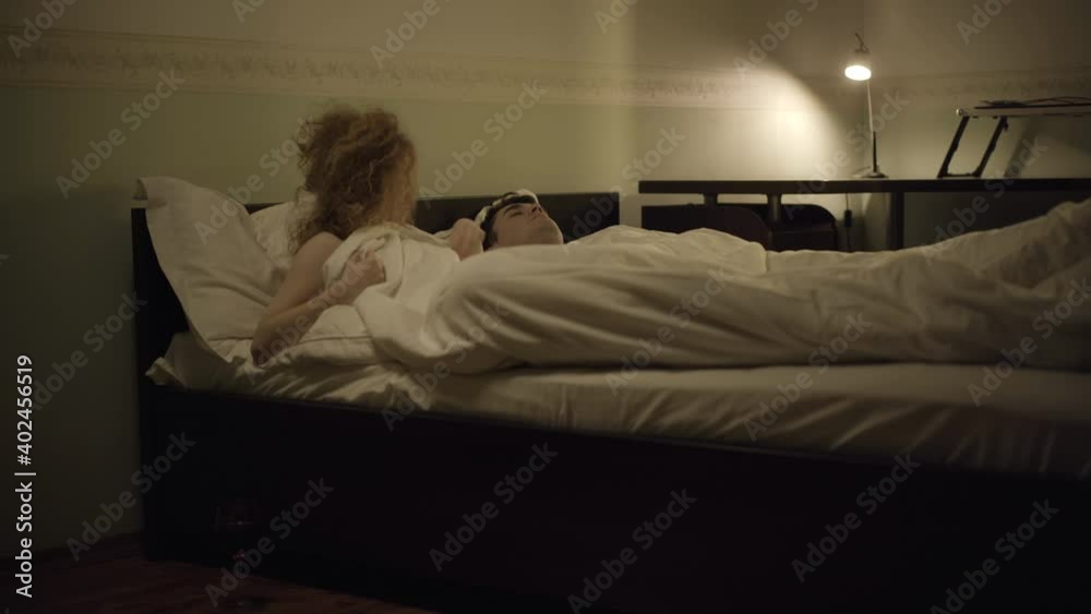 Wide shot of shocked woman waking up and checking naked man lying in bed. Wine glass standing on the floor. Embarrassed Caucasian lady lying in bedroom with stranger. Social concept. Wide shot of shocked woman waking up and checking naked man lying in bed. Wine glass standing on the floor. Embarrassed Caucasian lady lying in bedroom with stranger. Social concept.
