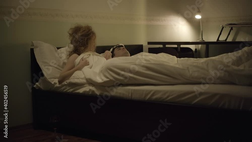 Wide shot of shocked woman waking up and checking naked man lying in bed. Wine glass standing on the floor. Embarrassed Caucasian lady lying in bedroom with stranger. Social concept. photo