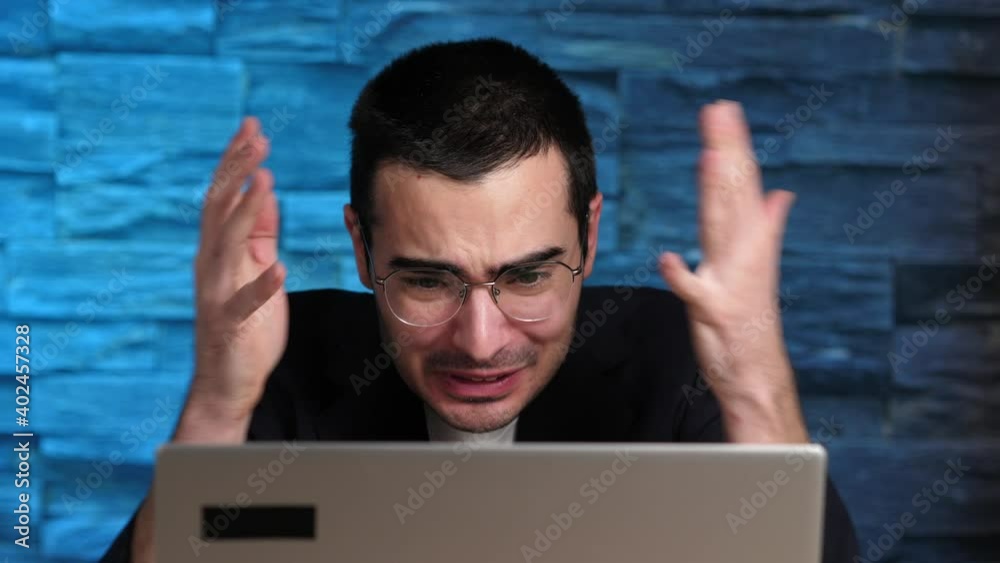Frustrated and furious young man in front of his laptop computer screen making many gestures.