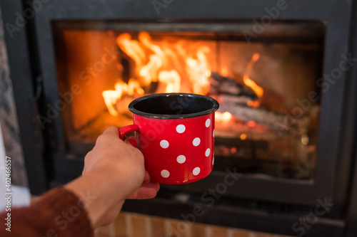 subjective view of a hand holding a red mug with white dots in front of the fireplace. winter concept.