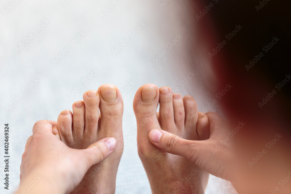 Fototapeta premium Horizontal over the shoulder closeup detail of yogini making forward bending exercise on the floor, reaching foot and touching toes with the hand. Indoor home yoga practice in sepia tone