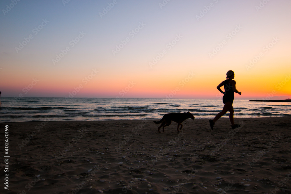 young woman running on a beach at sunset with her dog young woman running on a beach at sunset with her dog