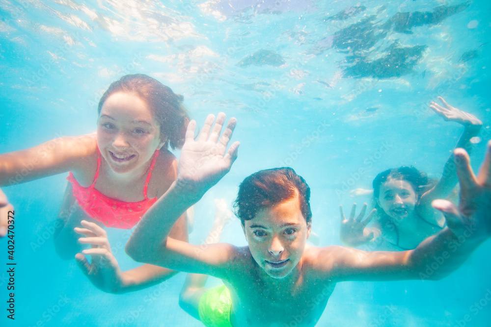 Group of three friends young kids dive underwater together waving hands and smiling
