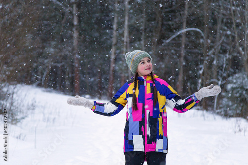 Cute happy teenage girl is catching snowflakes with her hands in winter forest