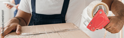 partial view of man holding scotch tape while packing box