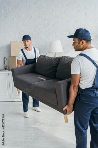 young multiethnic movers in caps and uniform carrying couch in apartment © LIGHTFIELD STUDIOS
