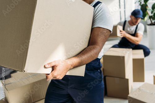 cropped view of indian mover holding carton box near coworker on blurred background photo