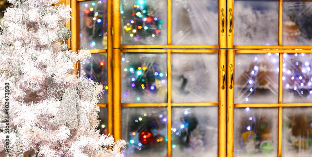 Naklejka premium Bright Christmas cards. White decorated Christmas tree and holiday lights through frozen glass. Holiday.