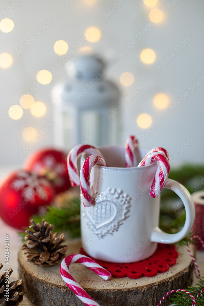 Tazza bianca con bastoncini di caramelle su tavolo di legno dove sono sparse decorazioni natalizie 