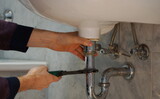 A close up of a hand holding a plumbing spanner screwing a fitting on wash basin waste pipe. 