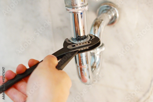 A close up of a hand holding a plumbing spanner screwing a fitting on wash basin waste pipe. 