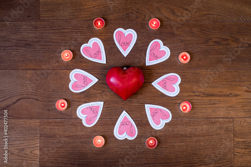 Red heart surrounded by eight pink paper hearts, with love written on them, eight burning candles, looking like a radiating flower, a shining rosette or the sun, on a wood background seen from above photo