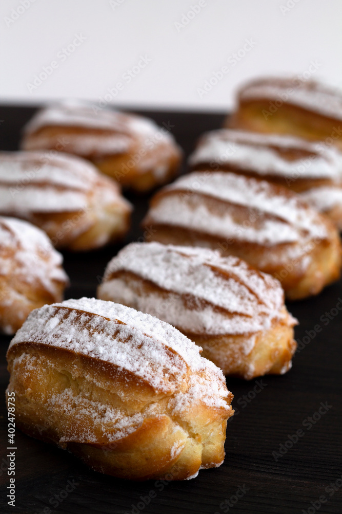 vanilla eclairs or profiteroles on a wooden table. Traditional french tasty dessert on dark background. copy space. vertical vanilla eclairs or profiteroles on a wooden table. Traditional french tasty dessert on dark background. copy space. vertical