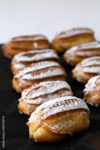 vanilla eclairs or profiteroles on a wooden table. Traditional french tasty dessert on dark background. copy space. vertical