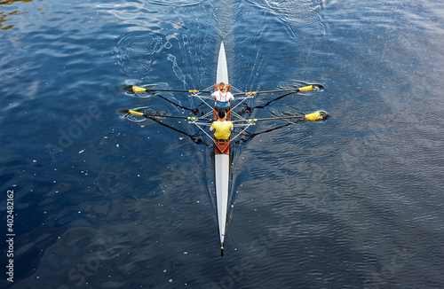A man and a woman are sculling in a rowboat on a river