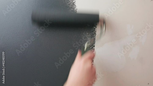 Roller paints the wall with gray paint. Craftsman applies gray paint to the wall using a roller.