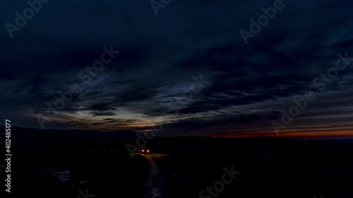 Timelapse at night of a dirt road and glare on the way from passing cars in the distance to driving in the sky are dark red moving clouds.
