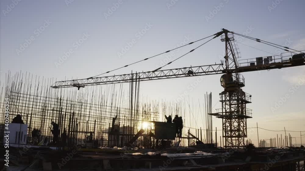 Panoramic view of builders silhouettes against the sky working on the top of the high block of flats under construction. Crane nearby. Aerial. Vladivostok, Russia Panoramic view of builders silhouettes against the sky working on the top of the high block of flats under construction. Crane nearby. Aerial. Vladivostok, Russia